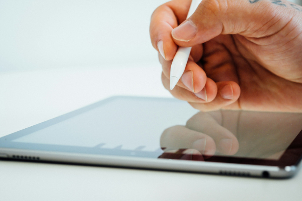 Main utilisant un stylet blanc sur une tablette graphique posée sur un fond clair
